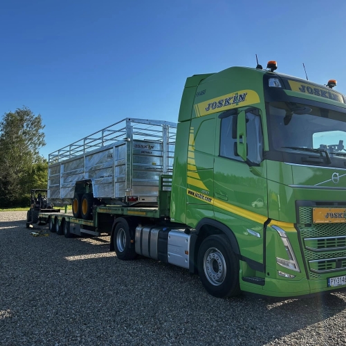 Joskin transportvogn læsset på grøn Volvo lastbil foran maskinhal