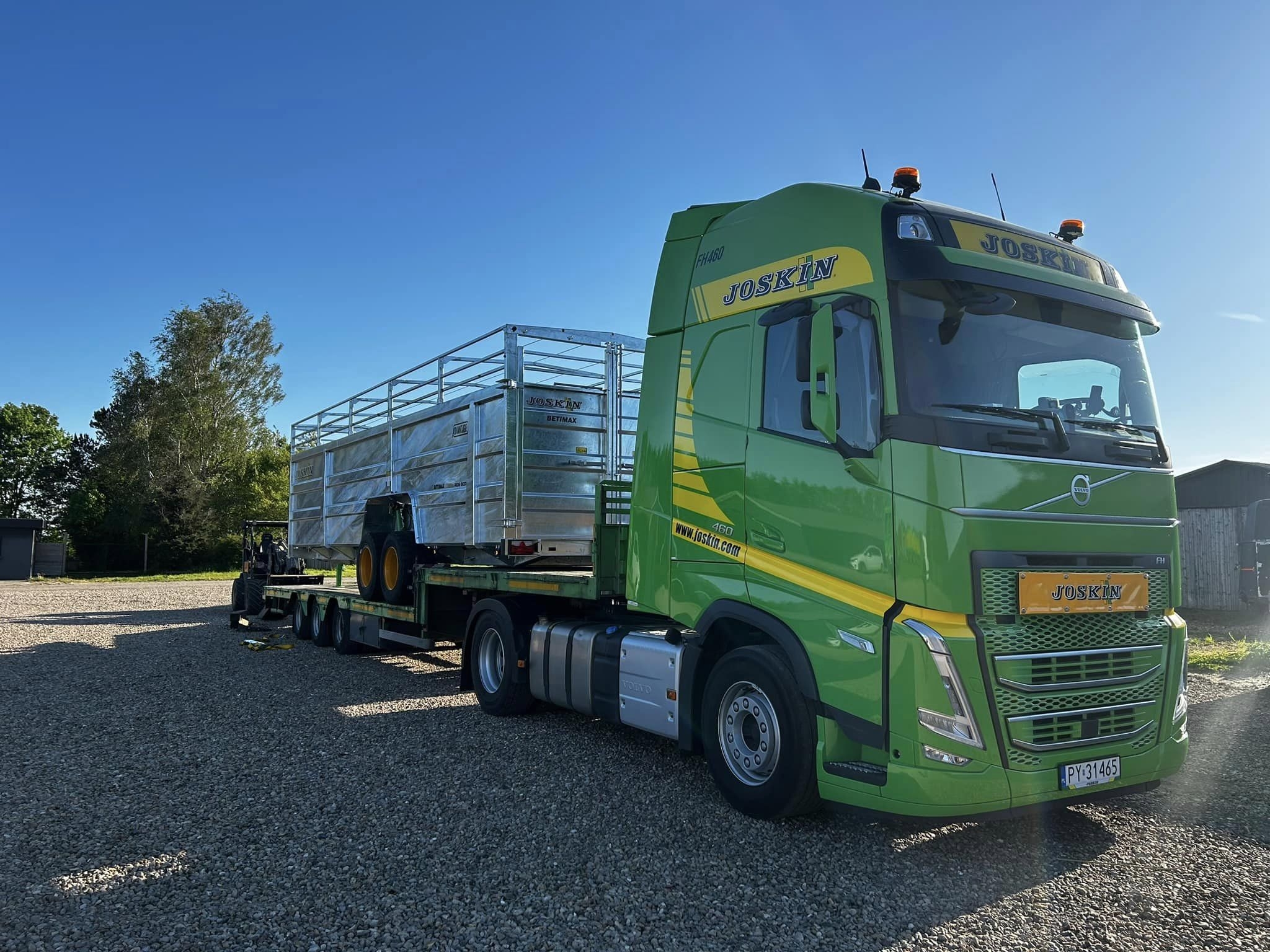 Joskin transportvogn læsset på grøn Volvo lastbil foran maskinhal